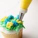 A person using an Ateco drop flower piping tip to frost a cupcake.