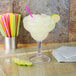 A GET customizable plastic margarita glass filled with a drink and a straw.
