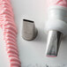 A white and silver Ateco Ribbon Piping Tip next to a pink icing tube with a pink ribbon on a counter.