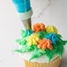 A cupcake with orange and green frosting piped to look like flowers using an Ateco Drop Flower piping tip.