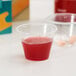 A Choice disposable medicine cup with red liquid and a pill in it.