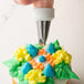 A person using an Ateco Drop Flower piping tip to decorate a cupcake with orange and white frosting.
