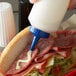 A person using a Vollrath Traex clear squeeze bottle with a blue cap to pour mayo on a sandwich.