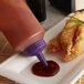 Fried chicken being dipped in red sauce using a Vollrath Color-Mate squeeze bottle with a purple cap.