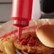 A hamburger with ketchup served on a counter in a farm-to-table restaurant with a Vollrath Traex red squeeze bottle on the counter.