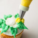 A cupcake with green frosting and yellow flowers piped on top using an Ateco drop flower piping tip.