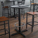 A Lancaster Table & Seating black cast iron bar height table base with a foot ring on a table with chairs.