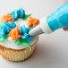 A person using an Ateco drop flower piping tip to frost a cupcake with a pastry bag.