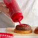 A hand using a Vollrath Color-Mate squeeze bottle to pour ketchup on a hamburger.