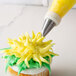 A cupcake with yellow frosting and a flower piped on top using an Ateco Drop Flower Piping Tip.