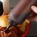 A hand holding a Vollrath Traex squeeze bottle of sauce pouring it onto a barbecue sandwich.