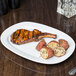 A CAC rectangular porcelain platter with steak and potatoes on a table.