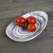An Elite Global Solutions Van Gogh black melamine oval plate with two tomatoes on it.