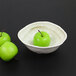 An Elite Global Solutions taupe melamine oval bowl filled with three green apples.