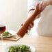 A person using an Acopa matte brown wooden pepper mill to season a salad.