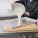 A chef pouring a white liquid mixture into a D&W Fine Pack foil sheet cake pan.