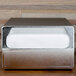 A silver rectangular countertop napkin dispenser with a white napkin in it.