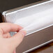 A hand pulling a napkin from a black Vollrath countertop napkin dispenser with a chrome faceplate.