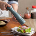 A person using an Acopa steel blue wooden pepper mill to grind pepper onto a salad.