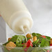 A person using a Vollrath Clear Twin Tip Squeeze Bottle to pour dressing on a salad.