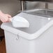 A person pouring milk from a white measuring cup into a white Cambro ingredient storage bin.