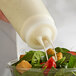 A person using a Vollrath Twin Tip squeeze bottle to pour white dressing onto a salad.