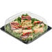 A Sabert plastic catering tray with sandwiches and vegetables in it with a high dome lid.