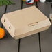 A Bagcraft Eco-Flute corrugated clamshell take-out box with a lid on a table.