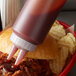 A person using a Vollrath Traex Twin Tip Squeeze Bottle to pour sauce on a pulled pork sandwich.