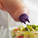 A hand holding a Vollrath Twin Tip Squeeze Bottle with purple liquid pouring into a salad.