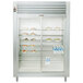 A Traulsen stainless steel reach-in refrigerator with two glass doors and shelves holding food.