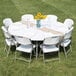 A Lancaster Table & Seating white plastic round folding table with white folding chairs and a vase of sunflowers.