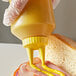 A person using a Vollrath Color-Mate squeeze bottle with a yellow cap to put mustard on a sandwich.