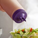 A hand using a Vollrath Twin Tip Squeeze Bottle with purple cap to pour dressing on a salad.