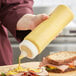 A hand using a Vollrath Traex squeeze bottle to pour mustard onto a sandwich.