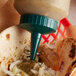 A plastic Vollrath squeeze bottle with a green cap pouring sauce into a tortilla.