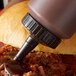 A brown plastic Vollrath bottle cap on a squeeze bottle of sauce on a burger.