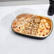A Durable Packaging black and gold aluminum foil entree take-out pan with cookies on a counter with a plastic lid.