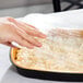 A hand using a plastic container to transfer food to a Durable Packaging Black and Gold aluminum foil pan with a dome lid.