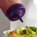A person using a Vollrath Traex purple bottle cap to pour dressing onto a salad.