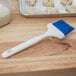 A Carlisle Sparta Spectrum blue pastry brush with a hook handle on a wood table.