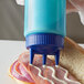 A close up of a blue Vollrath Tri Tip squeeze bottle with blue liquid being poured onto a sandwich.