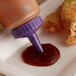 A purple Vollrath standard bottle cap on a brown sauce bottle being used to pour sauce on fried chicken.