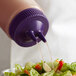 A Vollrath Traex purple Twin Tip bottle cap pouring liquid onto a salad.