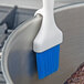 A Carlisle Sparta Spectrum Meteor pastry brush with blue bristles being used on a pan.