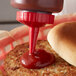 A Vollrath Traex red bottle cap pouring ketchup onto a hamburger.