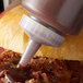 A close up of a clear plastic Vollrath sauce bottle with a white tip pouring sauce.