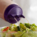A person pouring purple salad dressing from a Vollrath Tri Tip bottle onto a salad.