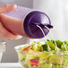A person using a Vollrath Tri Tip wide mouth squeeze bottle to pour dressing on a salad.