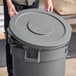 A person holding a Lavex gray commercial trash can lid.